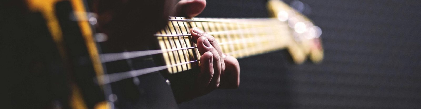 Person Playing Sun Burst Electric Bass Guitar in Bokeh Photography